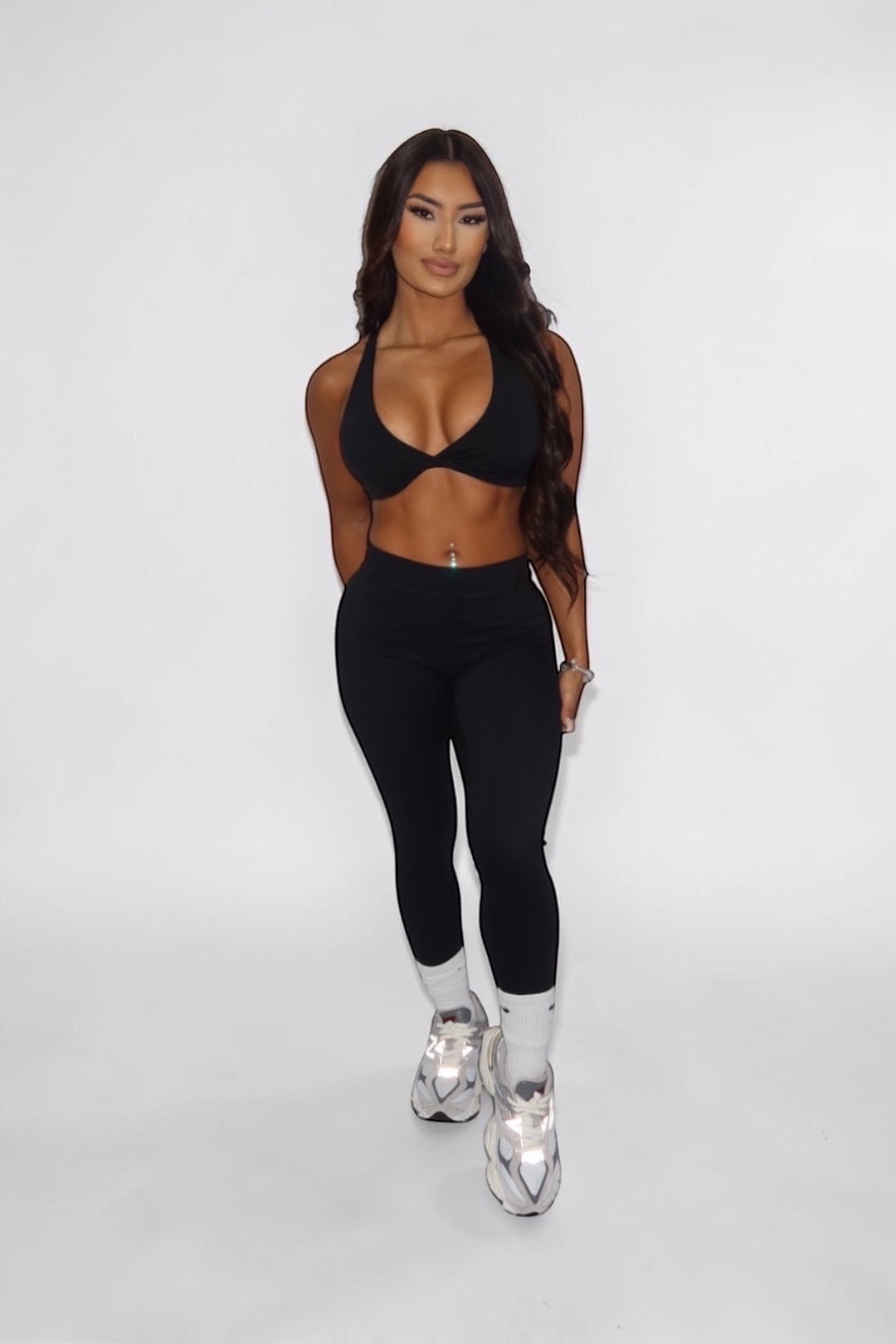 GLAMORZ black BBL bra worn by a woman with long dark hair, paired with matching black leggings and sneakers.