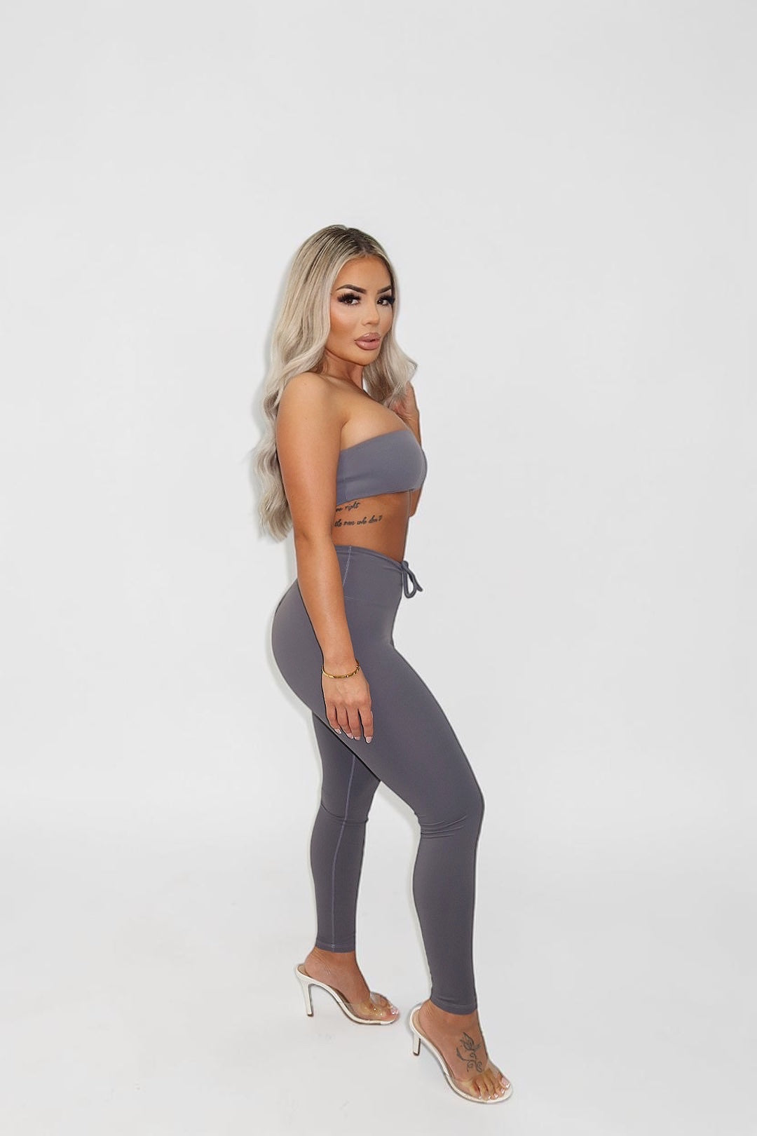 Model wearing GLAMORZ grey KHY scrunch leggings and matching bandeau top, side profile view.
